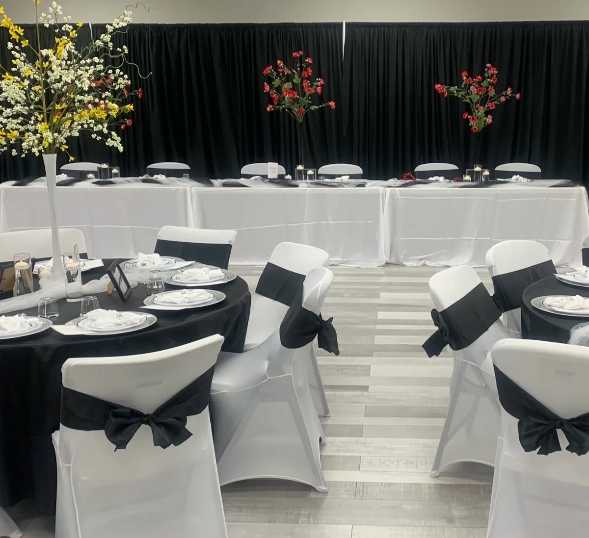 Grace Center event space in District Heights, MD set for a banquet with round tables, white chair covers with black sashes, tall floral centerpieces and a head table